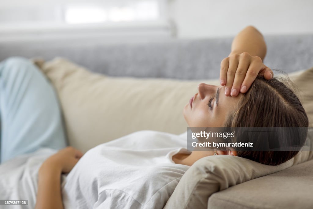Woman laying on sofa eyes closed feeling unwell