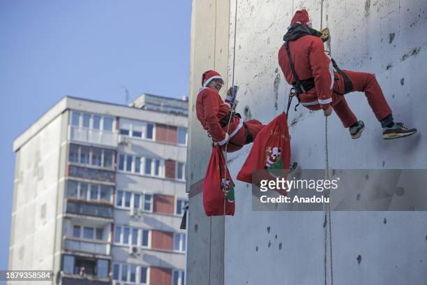 People dressed as the Santa Claus pass between two tall buildings and distribute gifts to the children ahead of New year's eve in Sarajevo, Bosnia...