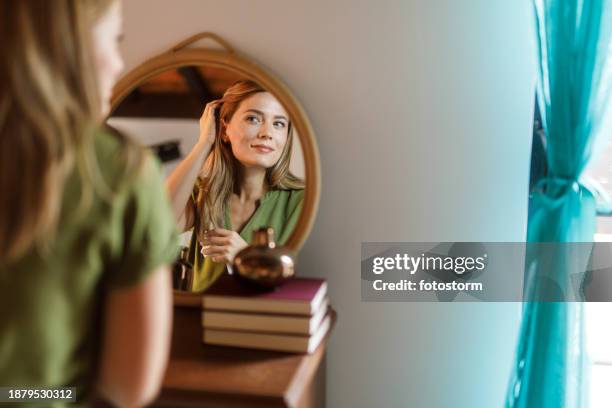 woman looking in the mirror and examining her skin and hair - body care and beauty stock pictures, royalty-free photos & images
