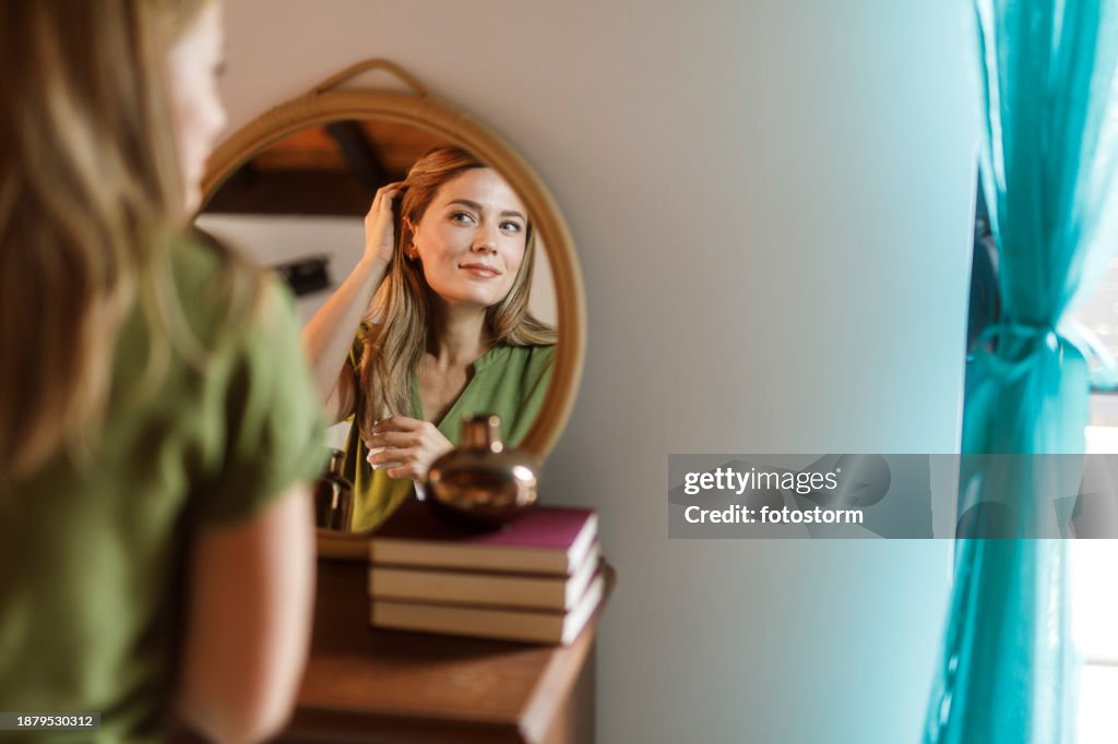 Woman looking in the mirror and examining her skin and hair