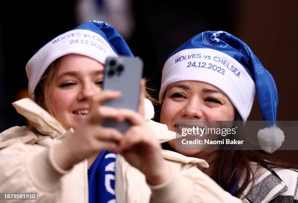 Fans of Chelsea pose for a photo as they take a selfie with a mobile phone, as they wear a Chelsea branded Blue Christmas Santa hat which reads...