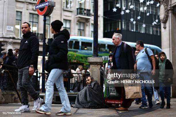 Members of the public carrying shopping bags walk past a rough sleeper at Oxford Circus in central London on December 27, 2023. Boxing Day footfall...