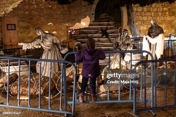 Palestinian girl stands next to art work "Nativity under the Rubble" by Palestinian artist Tariq Salsa in Manger Square near the Church of Nativity...