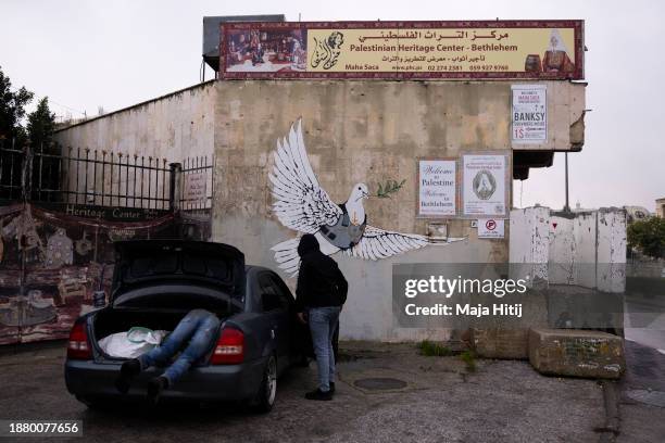 Palestinian man works in a car next to Banksy Dove mural on December 24, 2023 in Bethlehem, West Bank. Last month, Christian Palestinian leaders here...