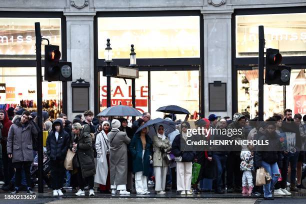 Shoppers stand in front of a window shop displaying a banner reading "Sale" as they prepare to cross the street, in central London, on December 27,...
