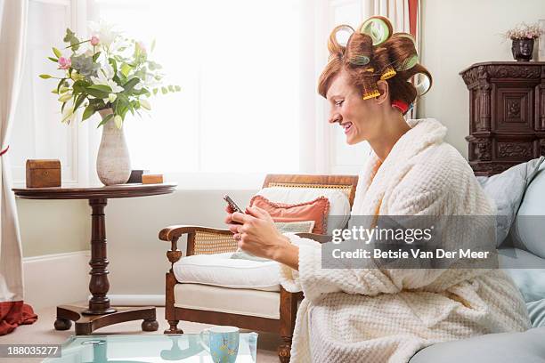 woman looking at phone, sitting with rollers in ha - hair curlers stock-fotos und bilder