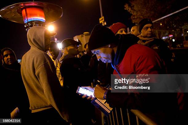 Warren Smart front, checks his smartphone as fans line up to attend the Sony PlayStation 4 midnight launch event in New York, U.S., on Thursday, Nov....