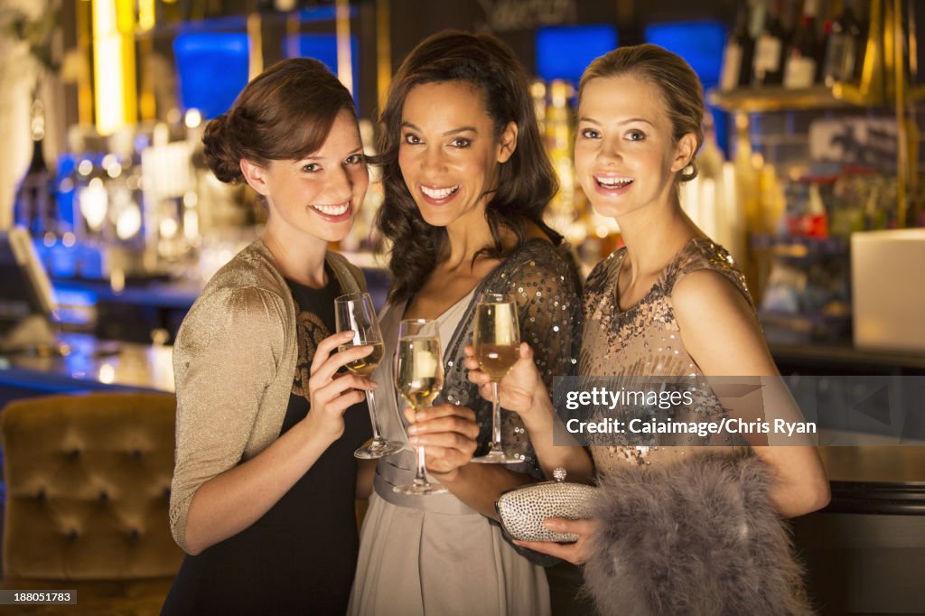 Portrait of well dressed women smiling with champagne flutes in luxury nightclub