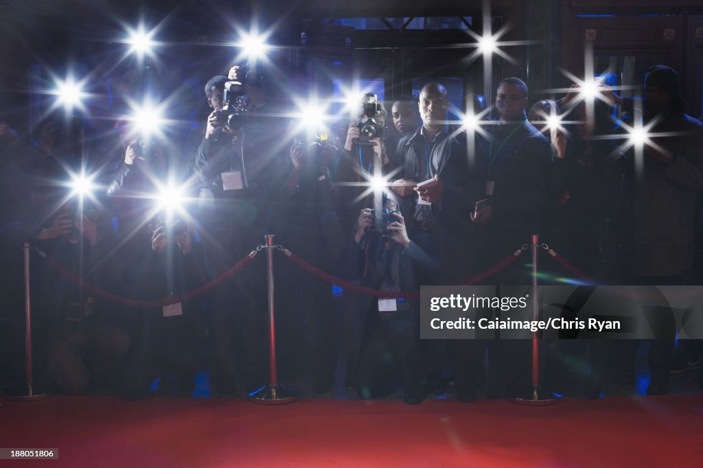Paparazzi using flash photography behind rope on red carpet