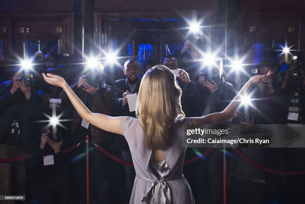 Rear view of female celebrity with arms outstretched to paparazzi at red carpet event