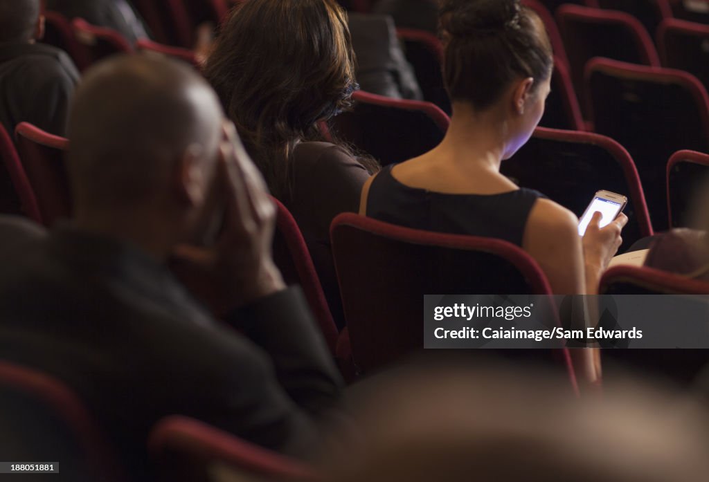 Vista posterior de la mujer mediante teléfono móvil en montaje tipo auditorio público