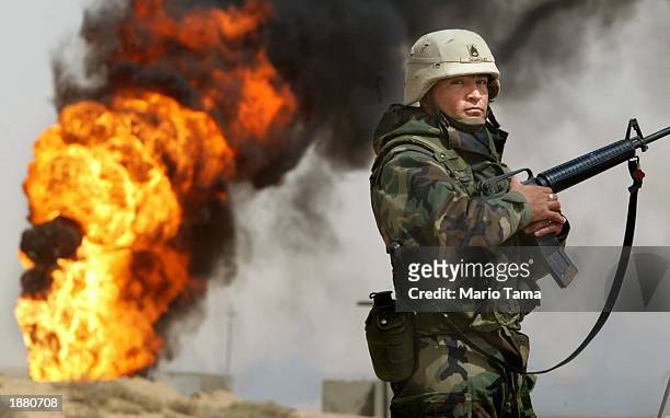 Army Staff Sergeant Robert Dominguez, of Mathis, Texas, stands guard next to a burning oil well at the Rumayla oil fields March 27, 2003 in Rumayla,...