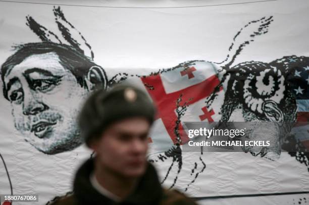 Policeman stands guard near a banner showing US President George Bush drawn as a ram butting Georgian President Mikheil Saakashvili sketched as a...