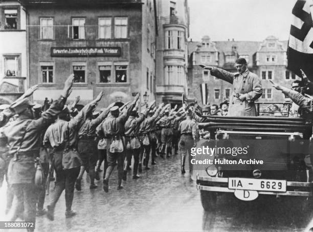 Nazi leader Adolf Hitler takes the salute as Sturmabteilung paramilitaries march past in the market square in Weimar, Germany, 13th November 1930. On...