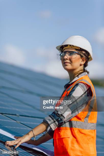 solar power sentinel: portrait of a young female electrical engineer ensuring peak performance with laptop and blueprint in a photovoltaic sun energy station farm - energy efficient building stock pictures, royalty-free photos & images
