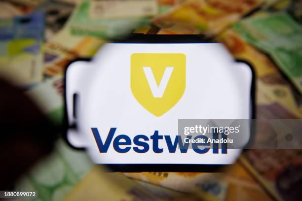 In this photo illustration, logo of Vestwell is displayed on mobile phone screen in front of the computer screen displaying Euro icon in Ankara,...