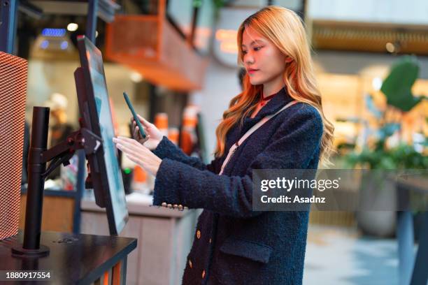 mujer asiática joven usando el móvil para el pago en el quiosco - kiosco fotografías e imágenes de stock