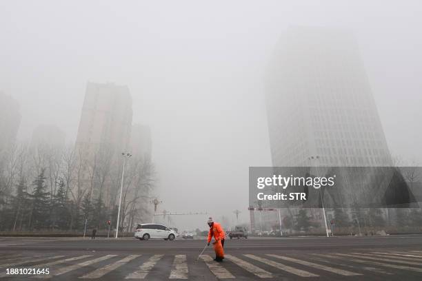 Street cleaner works as fog and air pollution shroud buildings in Qingzhou, in China's eatern Shandong province on December 28, 2023. / China OUT