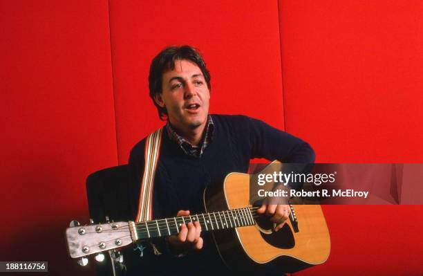 Portrait of British musician Paul McCartney as he plays acoustic guitar against a red background, October 7, 1984.