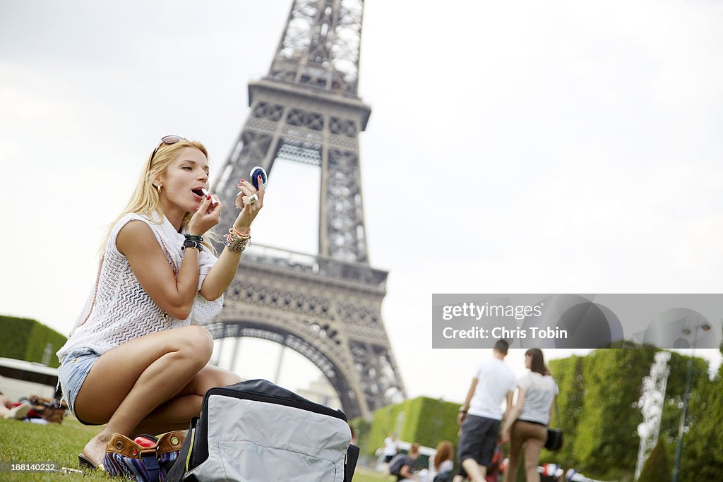 Young woman putting on makeup near Eiffel Tower