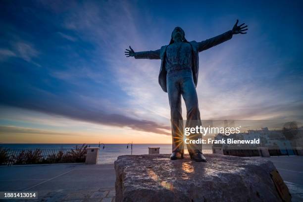 Statue of Domenico Modugno, the singer of the famous song Volare, houses of the small town in the distance, at sunrise.