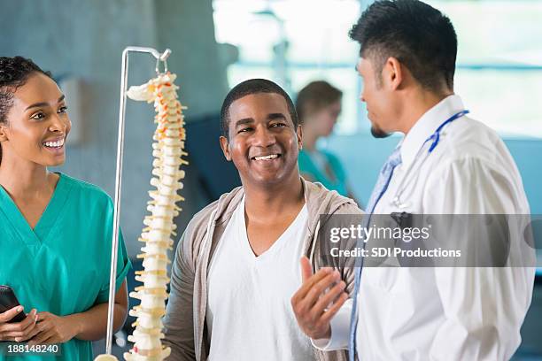 médico con la columna vertebral modelo hablar con sonriente pareja. - columna vertebral humana fotografías e imágenes de stock