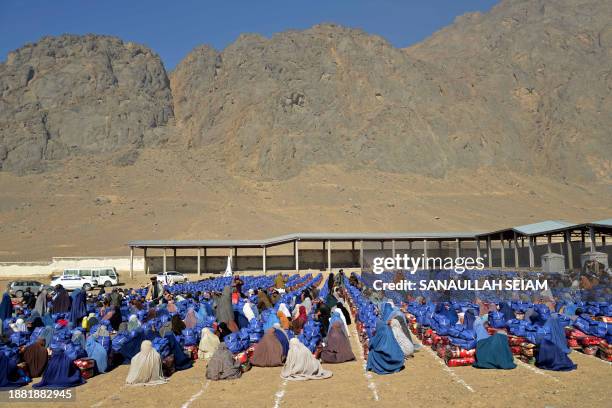 Afghan burqa-clad women sit next to winter and other goods aid distributed by a UMMAH charity in Kandahar on December 28, 2023.