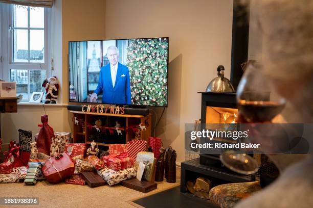 Above unopened Christmas presents, King Charles gives his first Christmas broadcast as monarch on a widescreen TV screen in the living room of a...