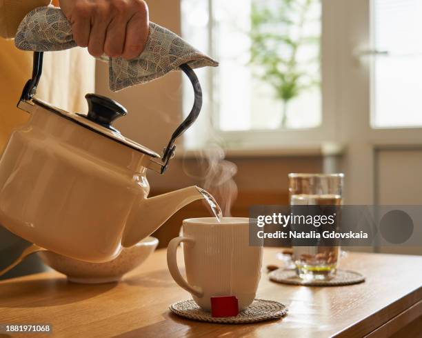 unrecognisable person making tea by pouring steaming boiling water into mug. - theepot stockfoto's en -beelden