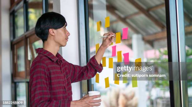 businessman planning to stick adhesive notes on a glass wall in the office - forgot something stockfoto's en -beelden