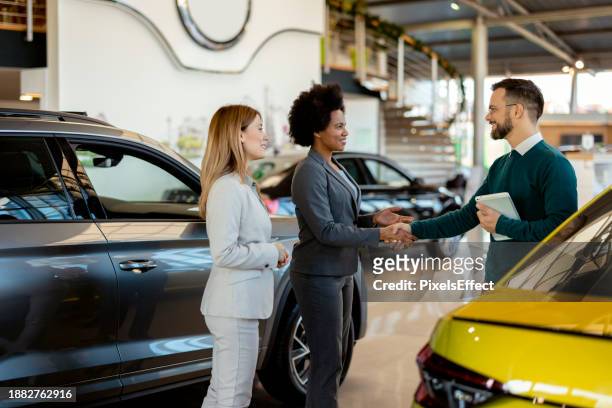 salesman shaking hands with female customer in dealership center - three people in car stock pictures, royalty-free photos & images