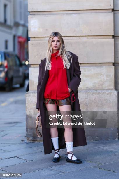 Natalia Verza wears a brown long oversized winter coat, a red sportswear jacket, a beige fluffy bag from Fendi, brown leather mini shorts, white...