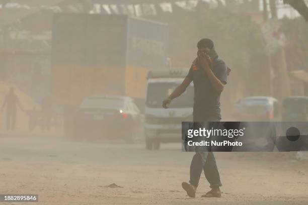 Man is walking on a dusty and heavily polluted road in Dhaka, Bangladesh, on December 2023.