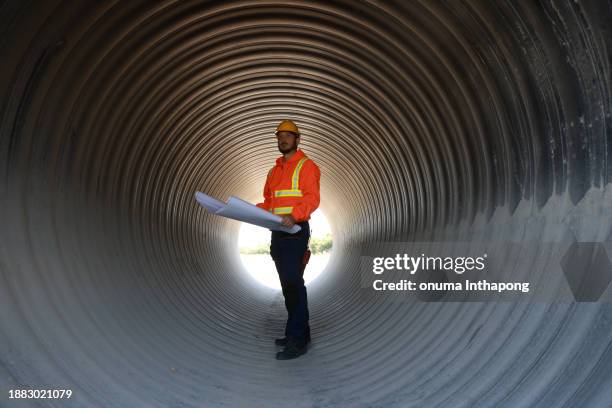 civil engineer with orange reflective safety jacket working in a huge tube at construction site line - pipeline stock pictures, royalty-free photos & images