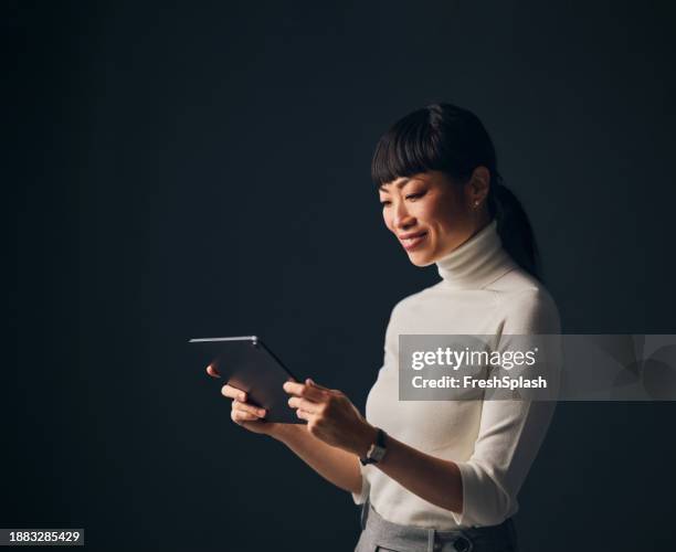 una hermosa mujer de negocios asiática feliz usando su tableta mientras está de pie contra un fondo gris - vestido blanco fotografías e imágenes de stock