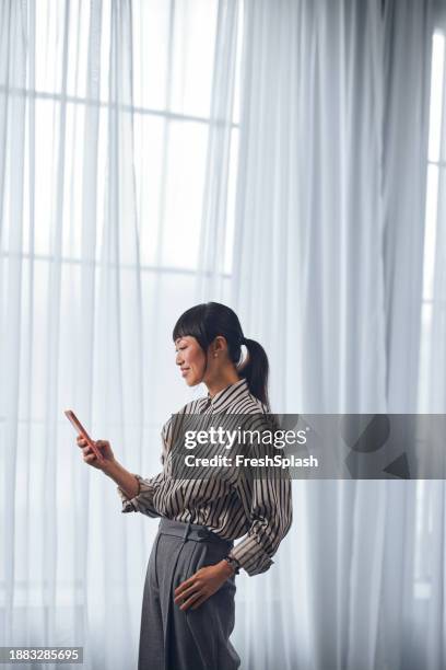 a happy beautiful asian businesswoman texting on her mobile phone while relaxing at home - striped shirt stock pictures, royalty-free photos & images