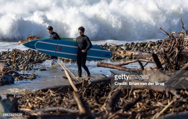 Ventura, CA Surfers navigate rocks and driftwood at Surfer's Point as they look for a spot to enter the water as large waves pound the beach on...