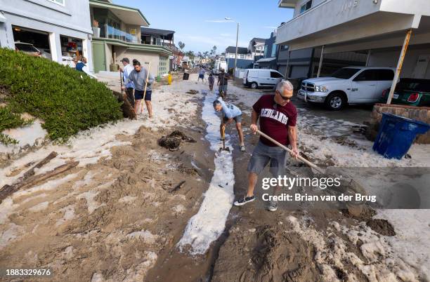 Ventura, CA Brad Steward, right, joins neighbors with shovels as they attempt to remove sand to allow water to drain after a seawall and sand berm...