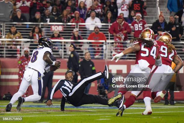 An official falls down as Lamar Jackson of the Baltimore Ravens is pressured by Fred Warner and Chase Young of the San Francisco 49ers during the...