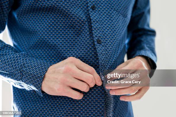 man buttons his shirt while getting dressed - camisa con botones fotografías e imágenes de stock