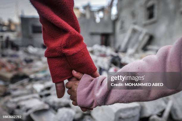 People hold hands as they inspect the damage on buildings destroyed during Israeli bombardment in Rafah on the southern Gaza Strip on December 29...