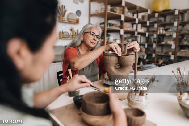 senior woman making a craft product on a ceramics workshop - vasijas de barro cocido fotografías e imágenes de stock