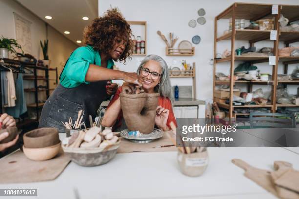 pottery teacher teaching student at a ceramics workshop - black sculptor stock pictures, royalty-free photos & images