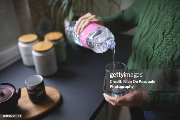 close up of a senior woman's hand filling a glass of water from a plastic bottle - purified water stock pictures, royalty-free photos & images