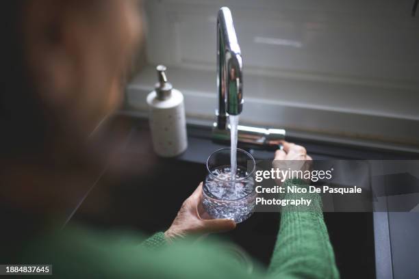 close up of a senior woman's hand filling a glass of filtered water right from the tap in the kitchen sink at home - filling stock-fotos und bilder