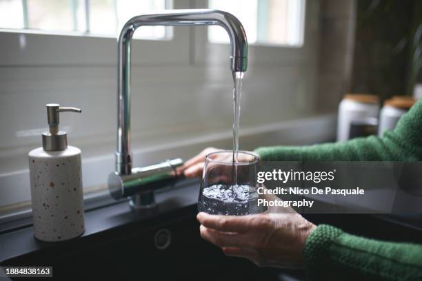 close up of a senior woman's hand filling a glass of filtered water right from the tap in the kitchen sink at home - süßwasser stock-fotos und bilder