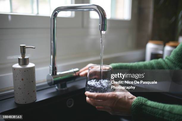 close up of a senior woman's hand filling a glass of filtered water right from the tap in the kitchen sink at home - auffüllen stock-fotos und bilder