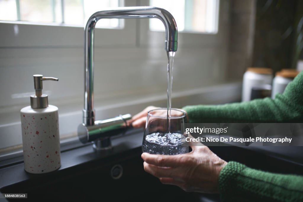 Close up of a senior woman's hand filling a glass of filtered water right from the tap in the kitchen sink at home