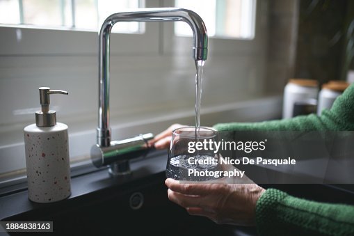 Close up of a senior woman's hand filling a glass of filtered water right from the tap in the kitchen sink at home Close up of a senior woman's hand filling a glass of filtered water right from the tap in the kitchen sink at home