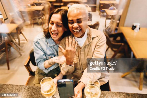 pareja de lesbianas en una videollamada o tomándose una selfie en un restaurante - gay engagement rings fotografías e imágenes de stock